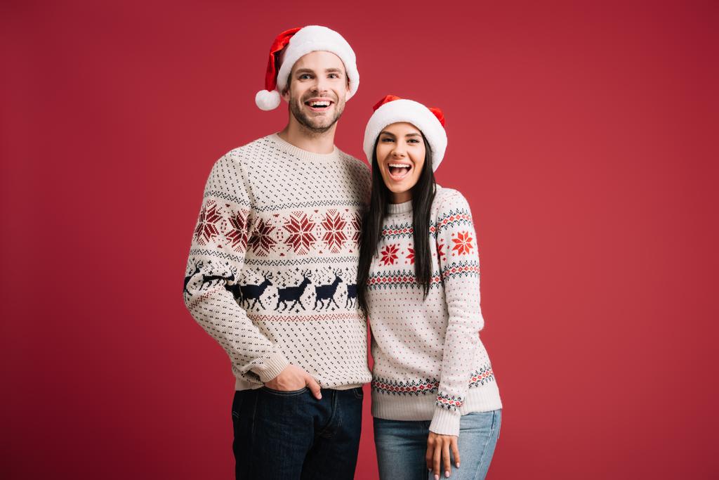 beau couple excité posant dans chapeaux Santa et pulls isolés sur rouge
 - Photo, image