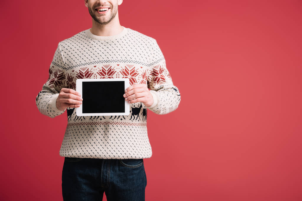 oříznutý pohled člověka v zimním svetru zobrazující digitální tablet s prázdnou obrazovkou, izolovaný na červenou - Fotografie, Obrázek