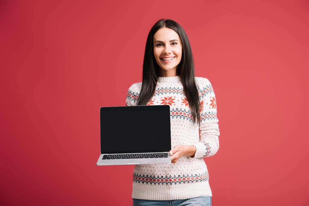happy woman in winter sweater showing laptop with blank screen isolated on red - Photo, Image