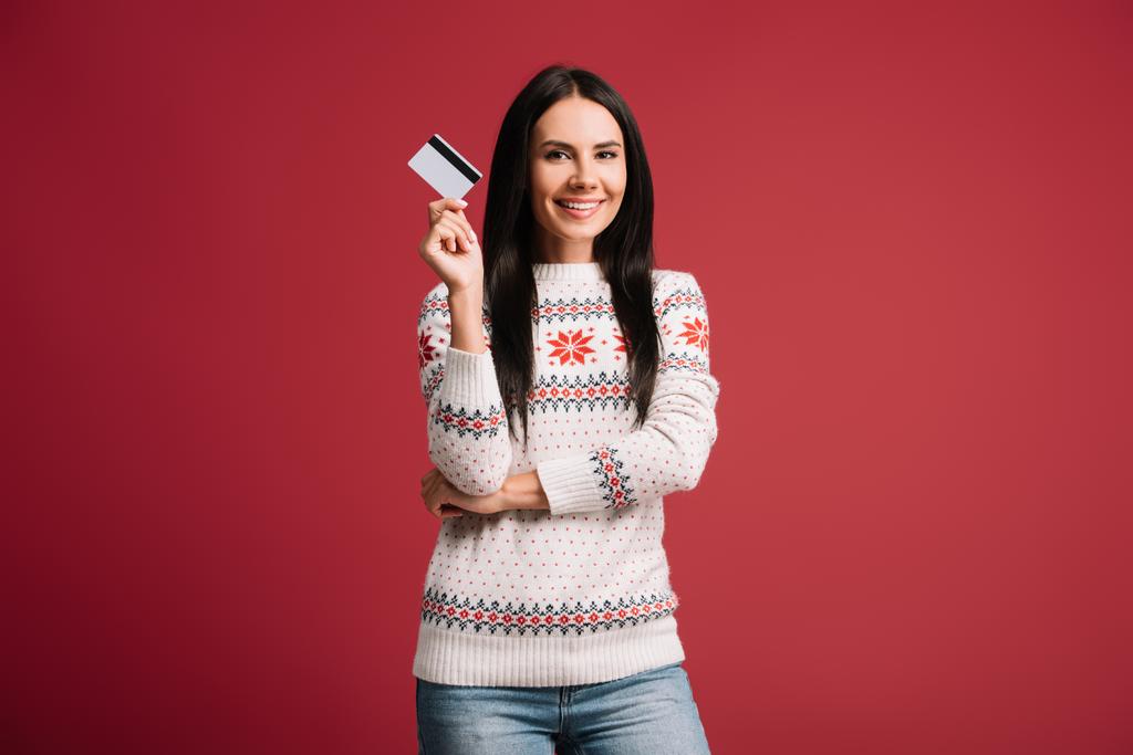 femme souriante en pull d'hiver tenant la carte de crédit, isolé sur rouge
  - Photo, image