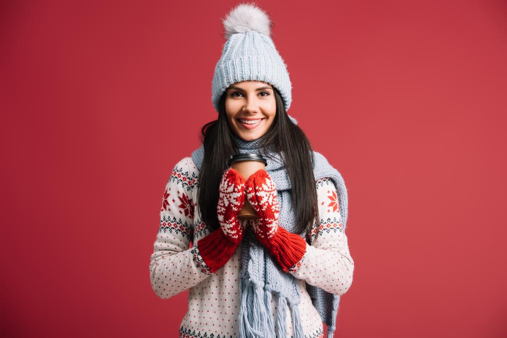 Žena v zimním klobouku, šálu a palčáku, která drží kávu, izolovaná na červenou - Fotografie, Obrázek