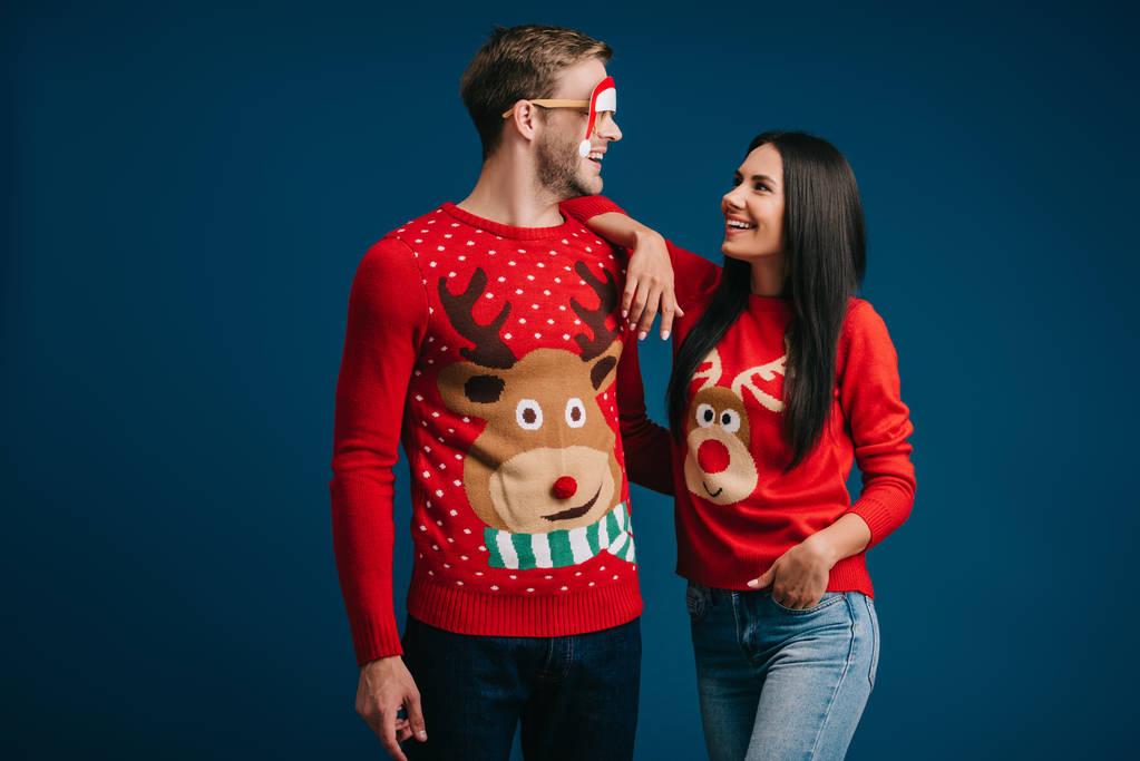 Lächelnder Mann mit Brille und Weihnachtsmann umarmt Freundin isoliert auf blauem Grund - Foto, Bild