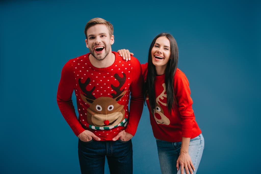 γέλιο ζευγάρι που ποζάρει Χριστουγεννιάτικα πουλόβερ απομονωμένη στο μπλε - Φωτογραφία, εικόνα
