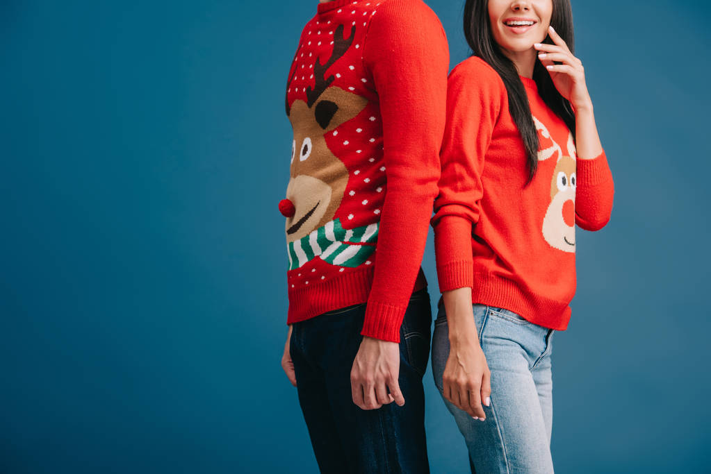 vista recortada de la pareja en suéteres de Navidad de pie espalda con espalda aislado en azul
 - Foto, Imagen