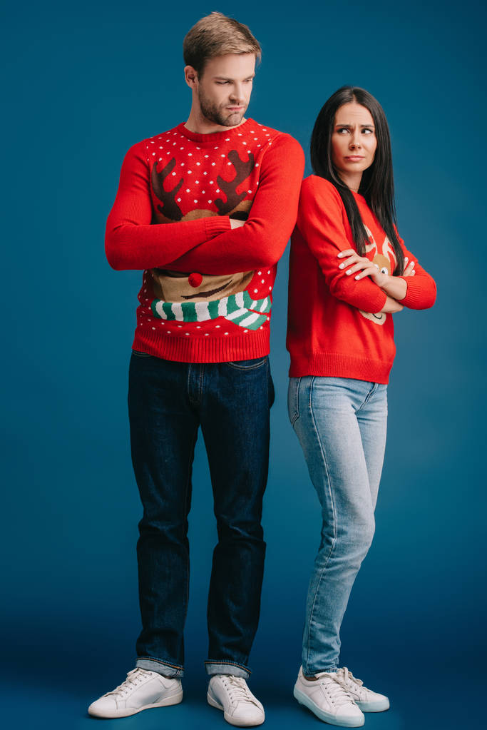 αναστατωμένος ζευγάρι σε χριστουγεννιάτικα πουλόβερ στέκεται με σταυρωτά όπλα απομονωθεί σε μπλε - Φωτογραφία, εικόνα