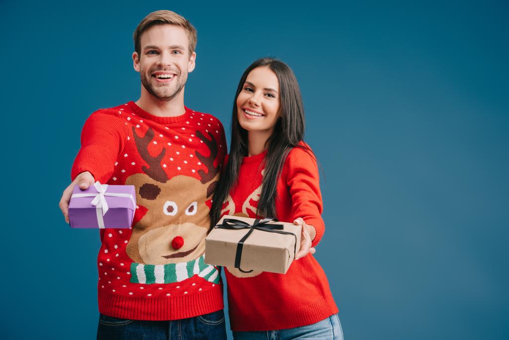 couple souriant en chandails rouges tenant cadeaux de Noël isolé sur bleu
 - Photo, image