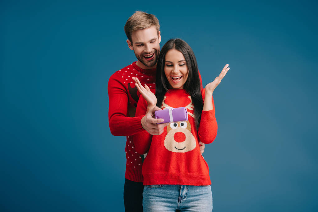 Glimlachende man presenteert kerstcadeau aan verrast vrouw geïsoleerd op blauw - Foto, afbeelding