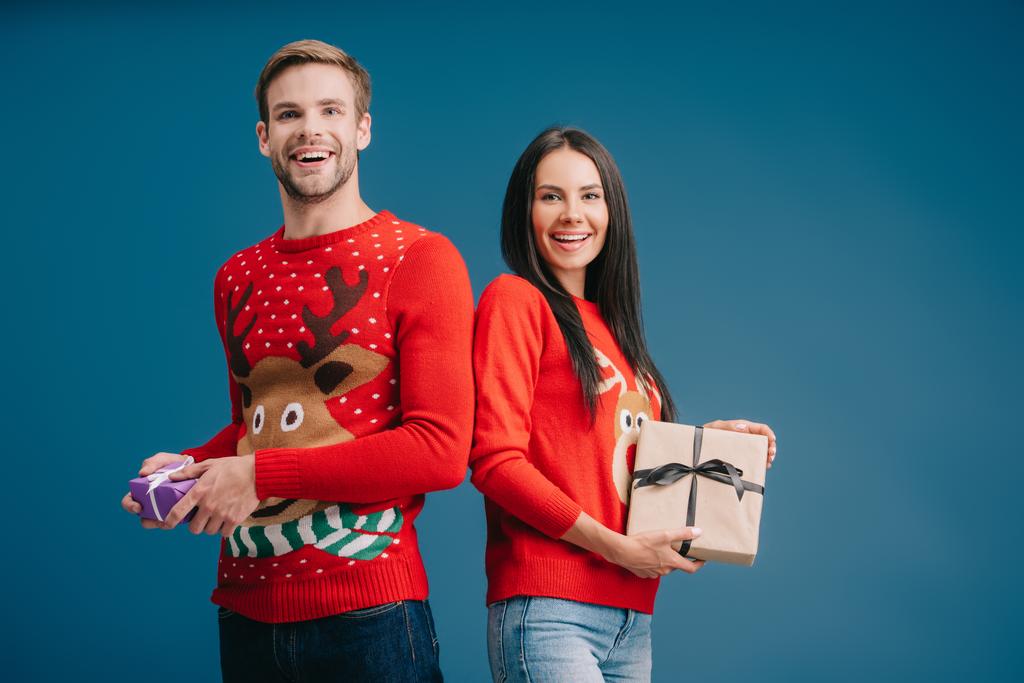 boldog pár piros pulóverek gazdaság karácsonyi ajándékok izolált kék - Fotó, kép
