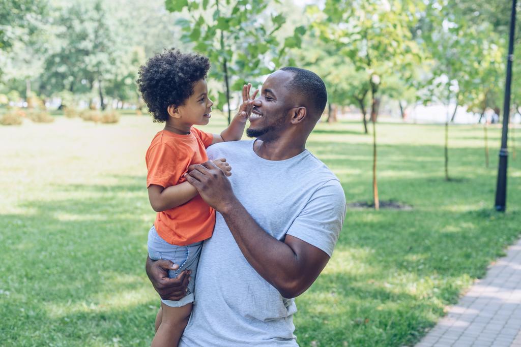 alegre afro-americano segurando adorável filho tocando seu nariz
  - Foto, Imagem