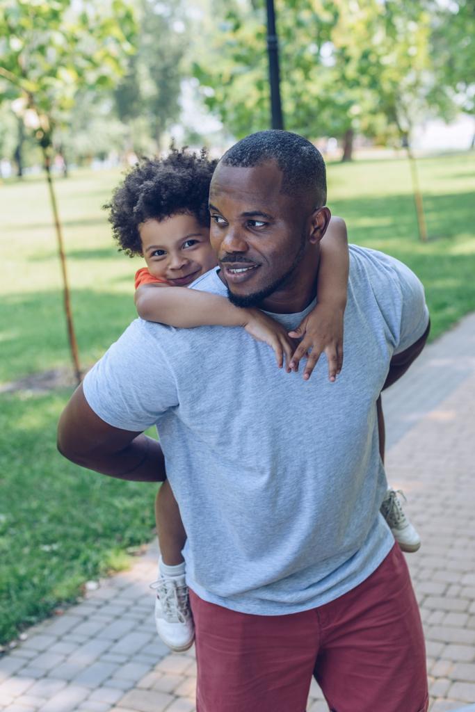 jovem africano americano pai piggybacking bonito filho enquanto caminhando no parque
 - Foto, Imagem