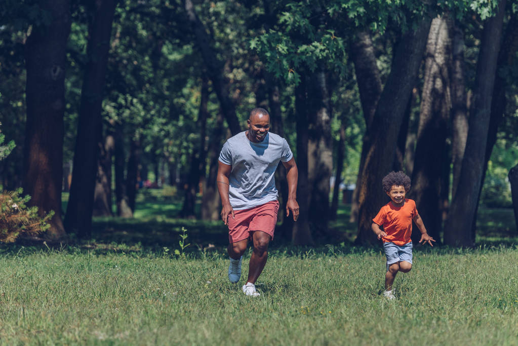 Χαρούμενος Αφρικάνος πατέρας και γιος τρέχουν ενώ διασκεδάζουν στο πάρκο - Φωτογραφία, εικόνα