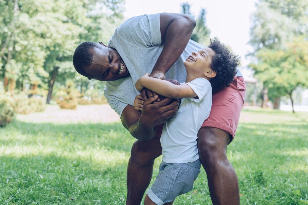 Genç Afrikalı Amerikalı baba parkta yakışıklı oğluyla rugby oynuyor. - Fotoğraf, Görsel