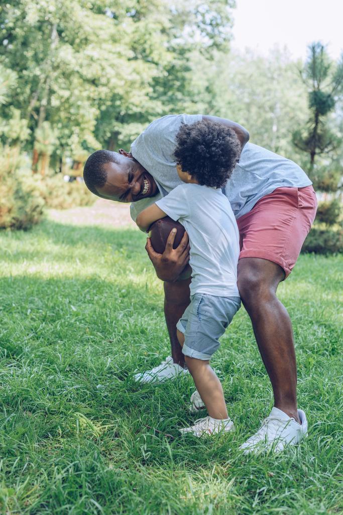молодой африканский американский отец играет в регби с очаровательным сыном в парке
 - Фото, изображение