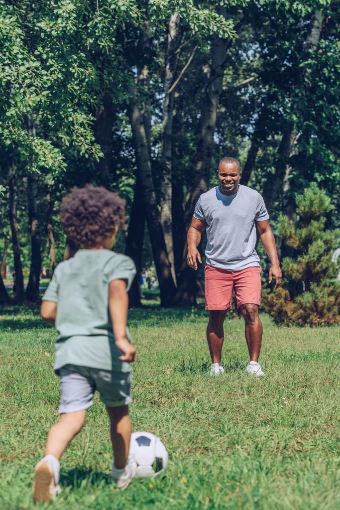 młody afrykański amerykański ojciec gra w piłkę nożną z uroczym synem w parku - Zdjęcie, obraz