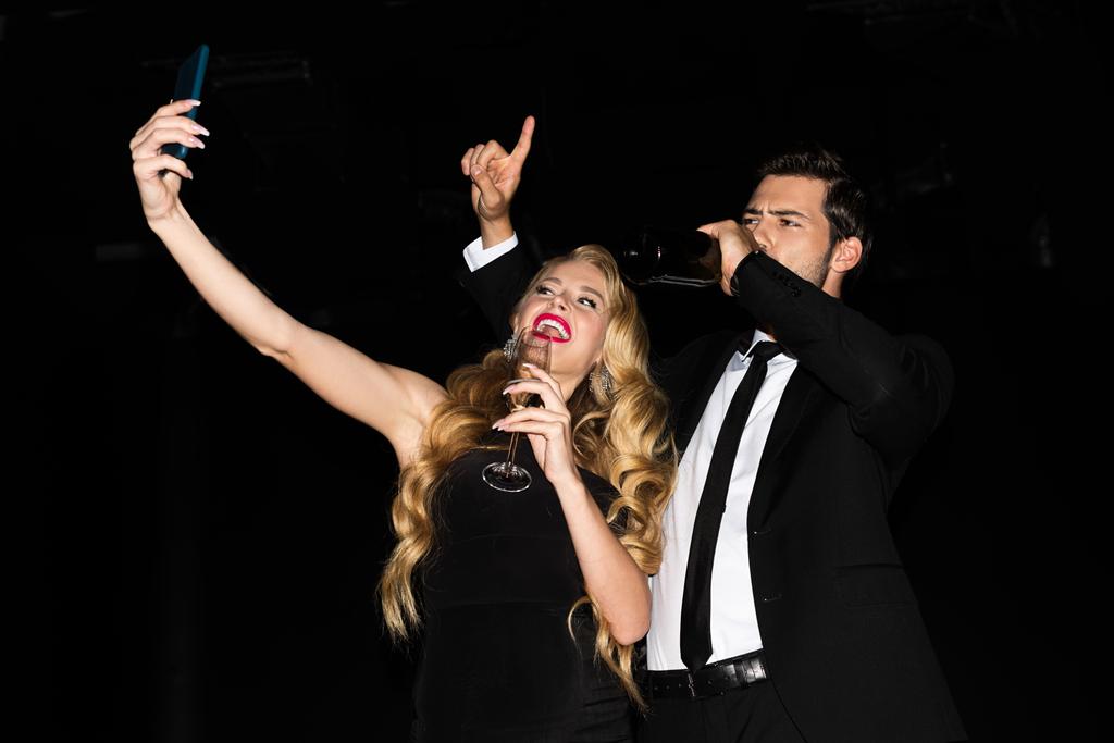 красивая девушка и парень делает селфи на смартфоне с очками на шампанском изолированы на черном
  - Фото, изображение