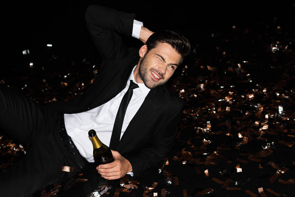 hombre elegante con botella de champán acostado en el suelo con confeti de oro para las vacaciones
 - Foto, imagen