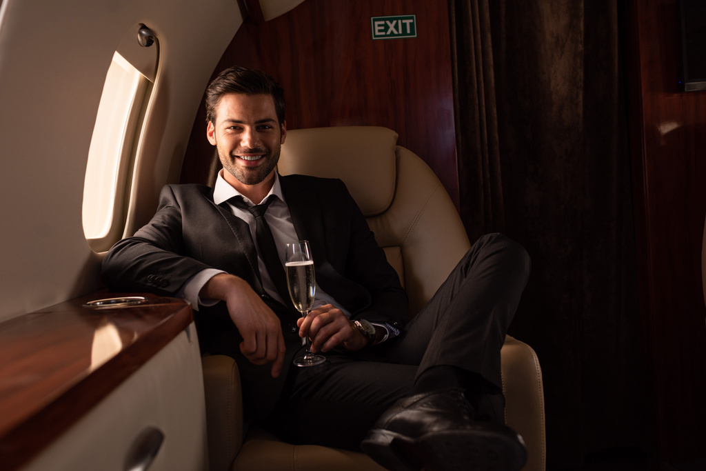 hombre sonriente guapo sosteniendo una copa de champán en avión
 - Foto, Imagen
