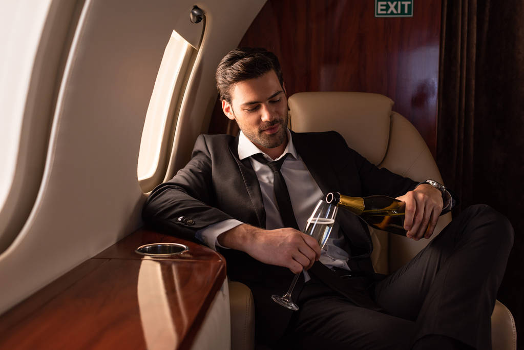 красивий чоловік у костюмі наливає шампанське в склянку в літаку
 - Фото, зображення