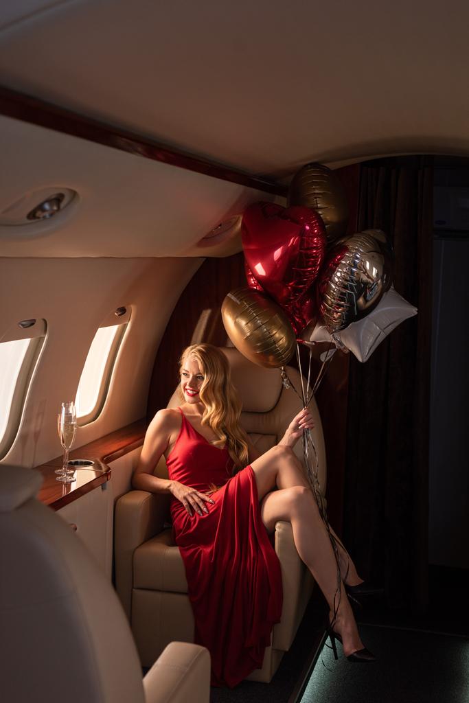 sexy aantrekkelijke vrouw met champagne en ballonnen zitten in vliegtuig - Foto, afbeelding