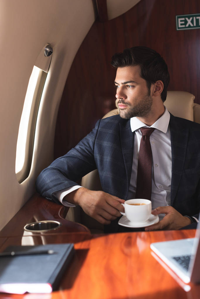 hombre de negocios confiado en traje que sostiene la taza de café en el avión durante el viaje de negocios
 - Foto, imagen