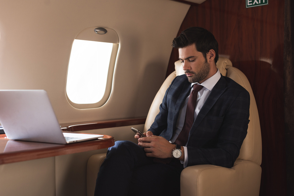 επιχειρηματίας που εργάζεται σε smartphone και φορητό υπολογιστή στο αεροπλάνο κατά τη διάρκεια επαγγελματικού ταξιδιού  - Φωτογραφία, εικόνα