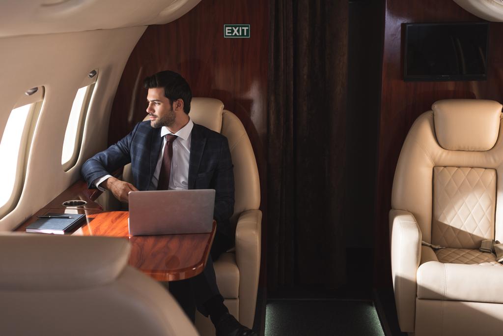 hombre de negocios guapo que trabaja con el ordenador portátil en avión durante el viaje de negocios
  - Foto, imagen