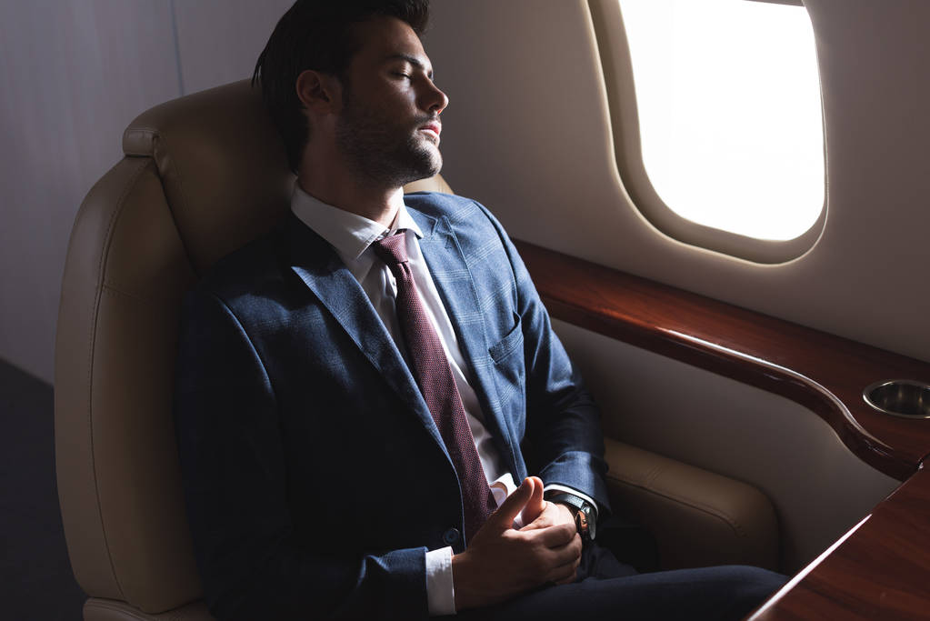 businessman sleeping in airplane during business trip - 写真・画像