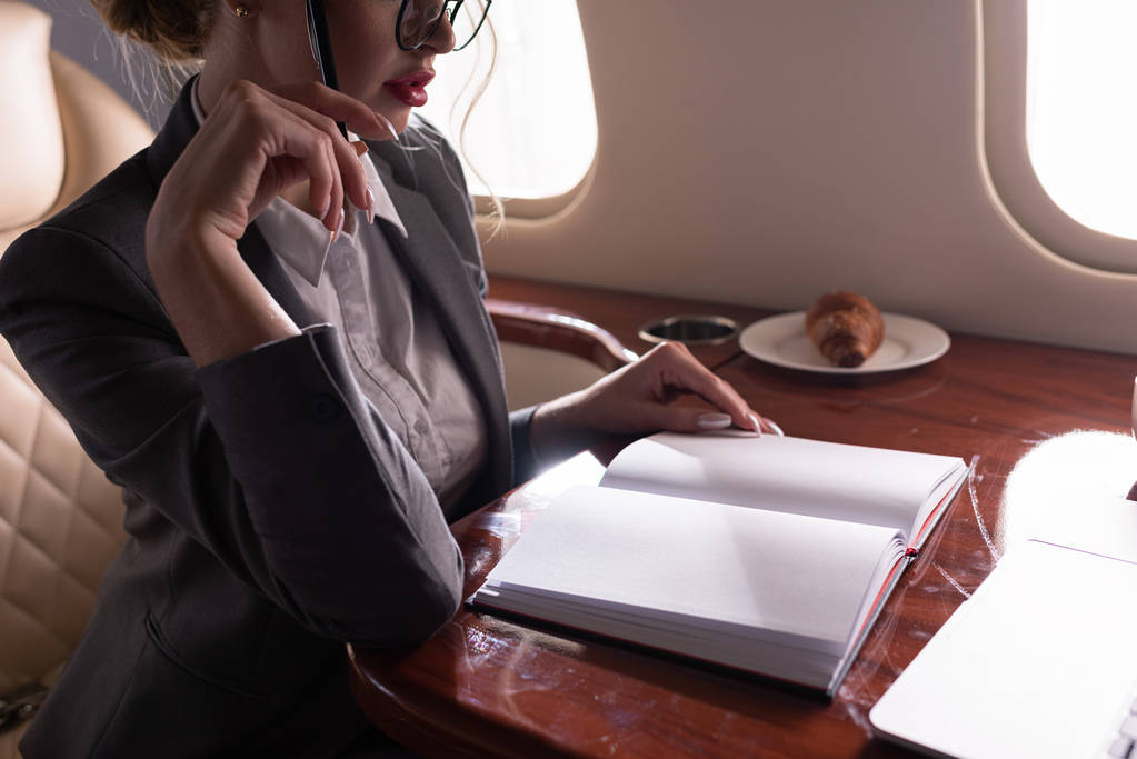 cropped view of businesswoman working with documents in plane during business trip - Photo, Image