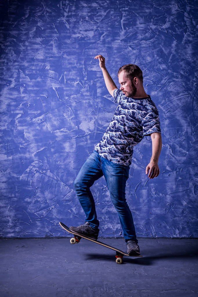 Skateboarder stojący na deskorolce na niebieskim tle. Ollie. - Zdjęcie, obraz