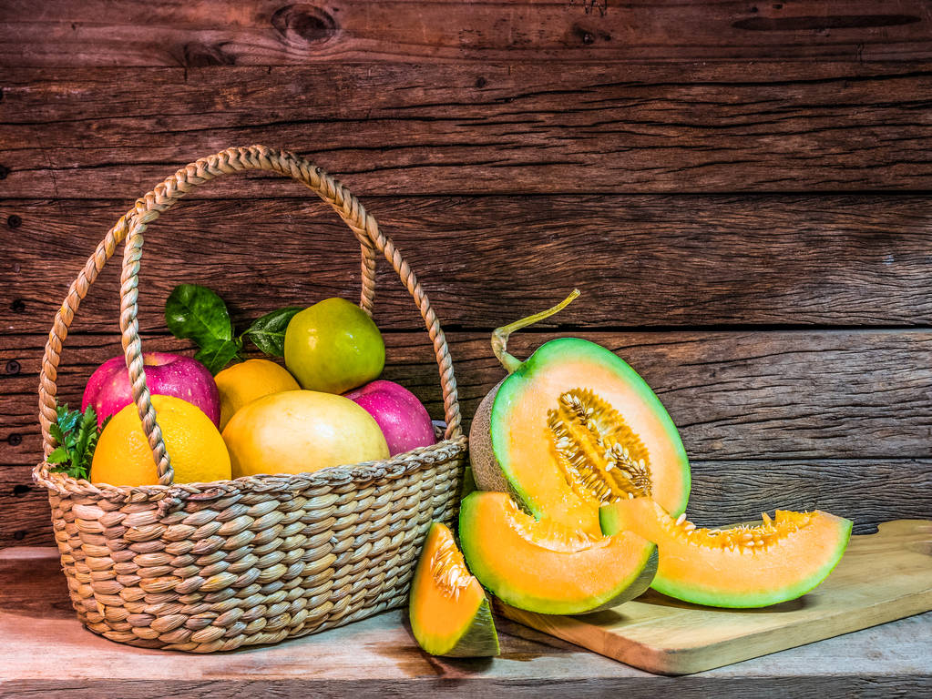 Cantaloupe-Melonenscheiben auf einem Holzteller mit einem Obstkorb - Foto, Bild