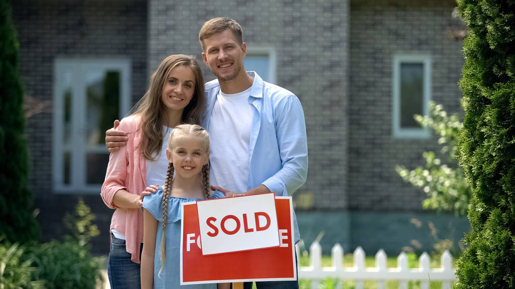 Szczęśliwa rodzina gospodarstwo sprzedawane znak, stoi przed nowym domu kupił, kciuki w górę - Zdjęcie, obraz