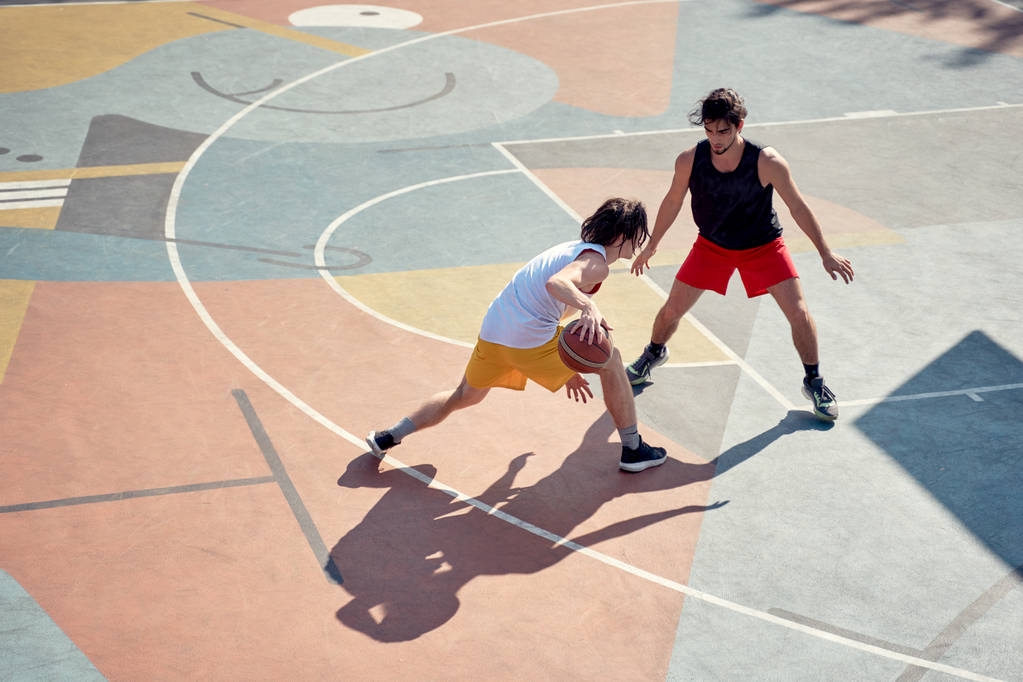 Obraz z góry widok dwóch młodych sportowców mężczyzn gra w koszykówkę na placu zabaw w godzinach porannych. - Zdjęcie, obraz
