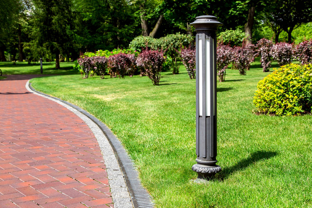 ground street lantern near winding footpath alley with a drainage system and a walkway on park with trees along a lawn with a green grass and bushes on well maintained park, nobody. - Photo, Image