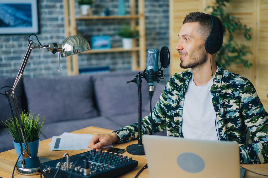 Радісний хлопець розмовляє в мікрофонах у навушниках, використовуючи ноутбук у студії
 - Фото, зображення