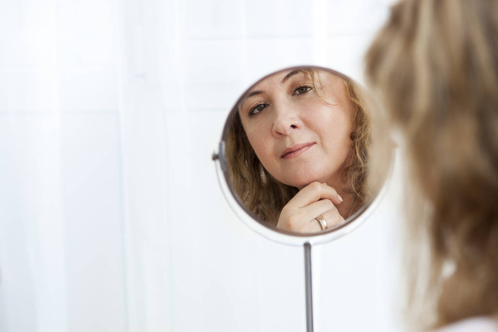 Красивая здоровая белая женщина смотрит в зеркало
 - Фото, изображение
