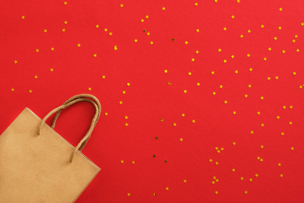 Christmas banner. Background Xmas design of craft paper shopping bag and glitter golden confetti on red background. Christmas poster, greeting card, header, social media banner. Christmas sale concept - Photo, Image