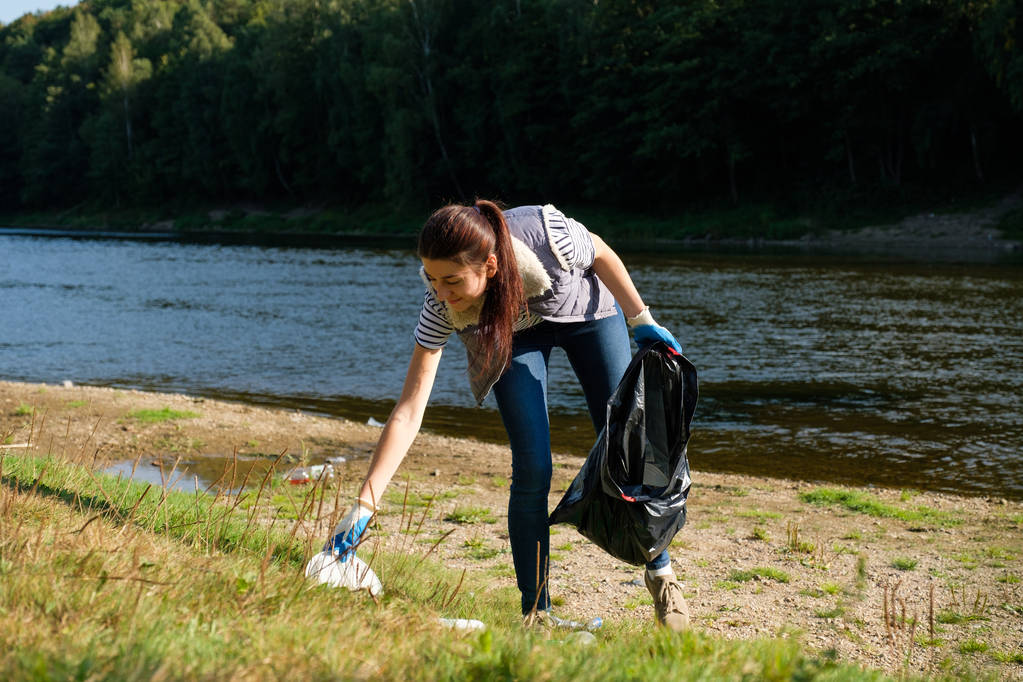 Eine freiwillige Frau sammelt Plastikmüll am Ufer des Flusses. Umweltkonzept zur Reinigung - Foto, Bild