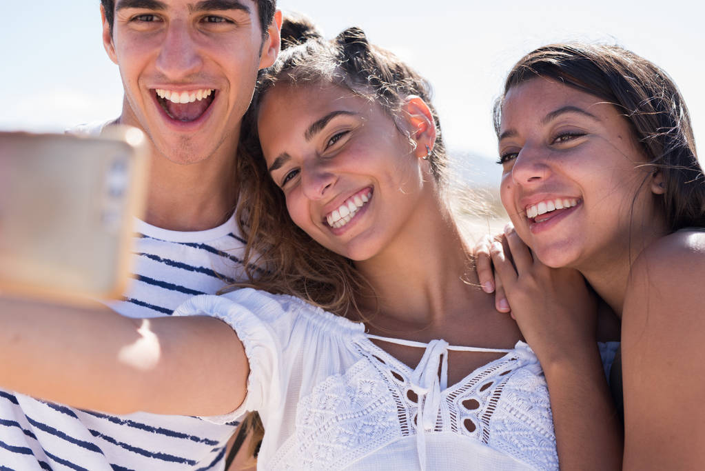 Três jovens millennial pessoas, duas meninas e um menino estão posando e olhando para a câmera e sorrindo
 - Foto, Imagem