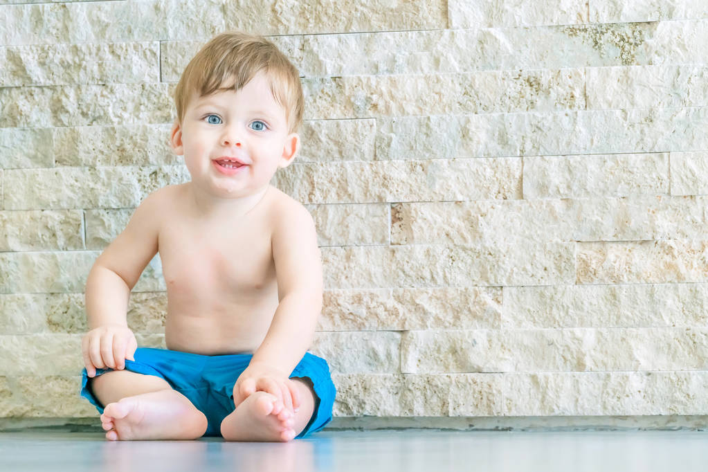 石の近くの床に座って青い目のブロンドの赤ん坊を微笑むw - 写真・画像