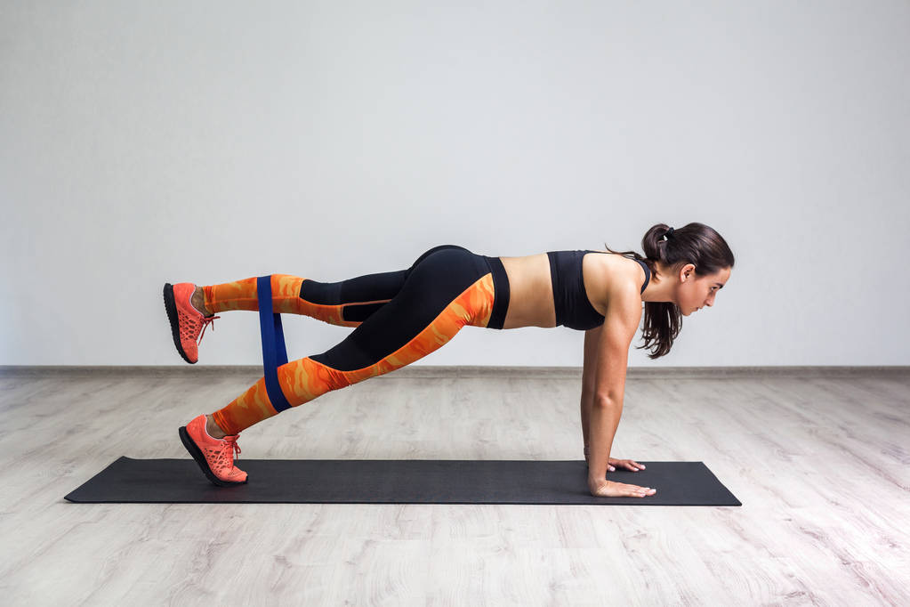 Вид сбоку сильной атлетичной молодой белой женщины в спортивной одежде лежащей на коврике и тренировочных ногах и ягодицах мышцы при использовании фитнес-эластичной ленты в тренажерном зале
 - Фото, изображение