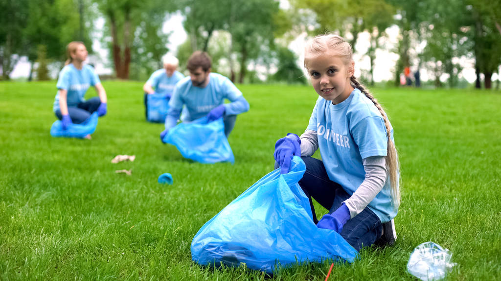 Nätti koulutyttö auttaa vapaaehtoisia keräämään roskia pusseihin puistossa
 - Valokuva, kuva