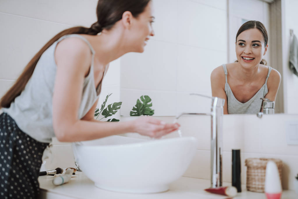 Hymyilevä houkutteleva nainen katselee peiliin kylpyhuoneessa
 - Valokuva, kuva