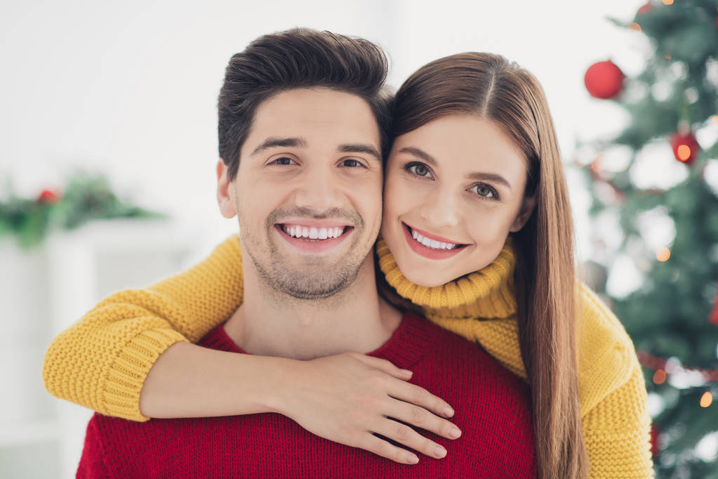 Крупним планом фото двох позитивних веселих романтиків, які обіймають стерво, насолоджуються вечіркою різдвяного часу, відчувають ніжний зв'язок у будинку з новорічним орнаментом у приміщенні
 - Фото, зображення