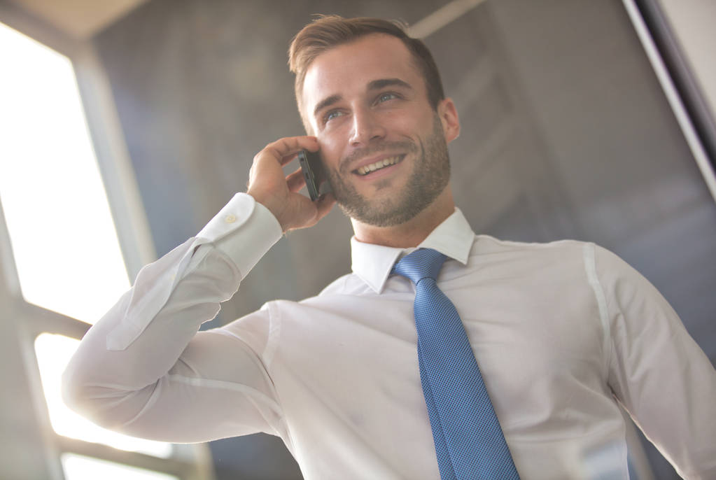 Handsome young businessman smiling while talking on smart phone  - Photo, Image