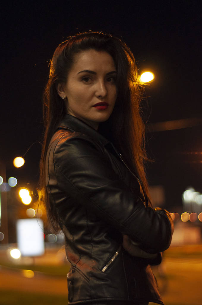 Straßenstil, Mode. Porträt einer Frau in Schwarz mit schönem Make-up und rotem Lippenstift auf der Straße mit Gegenlicht, hellen Lichtern und Laternen-Licht - Foto, Bild