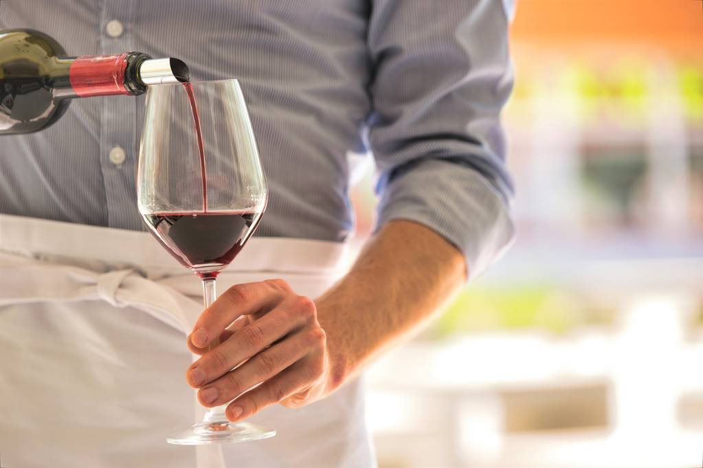 Розріз офіціанта, що поливає червоне вино в келиху в ресторані
 - Фото, зображення