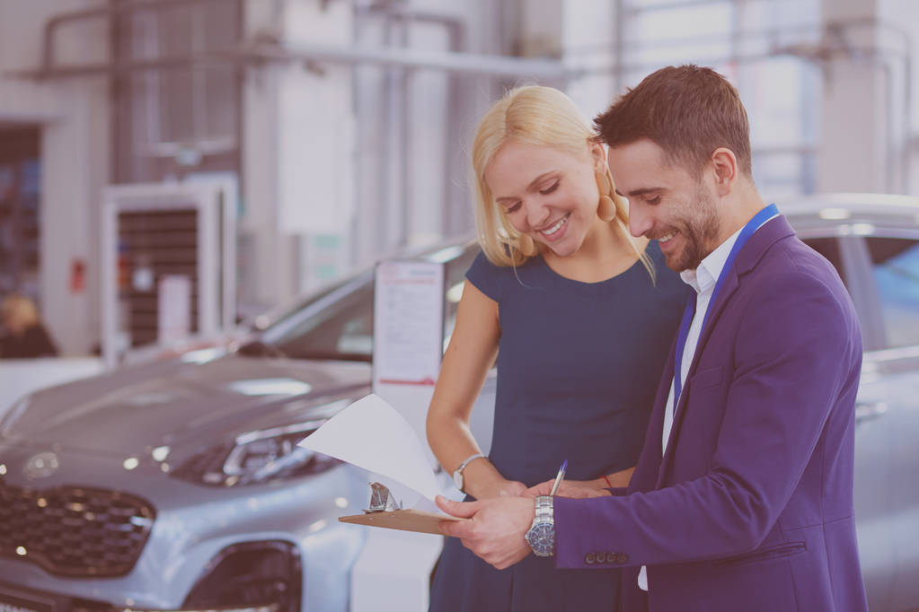 Продавец автомобилей продает автомобиль счастливому клиенту в автосалоне и передает ключи - Фото, изображение