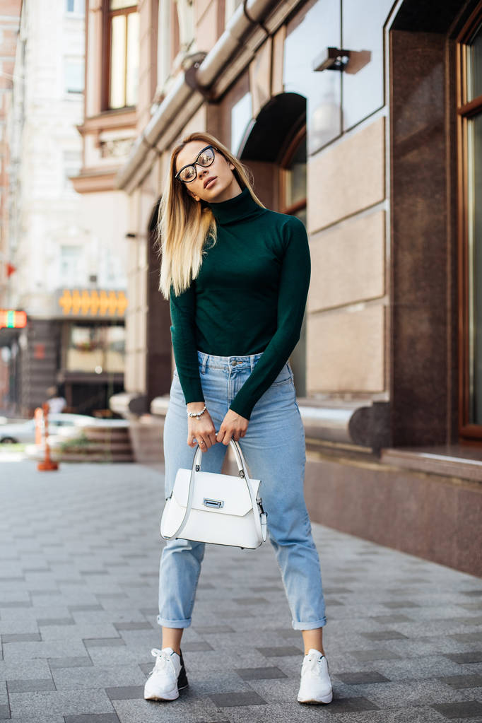 Outdoor lifestyle fashion portret van vrij elegante glamour blonde vrouw met lange benen, het dragen van trendy sneakers, jurk trui en jas, poseren in Europa stad, reizen alleen. - Foto, afbeelding
