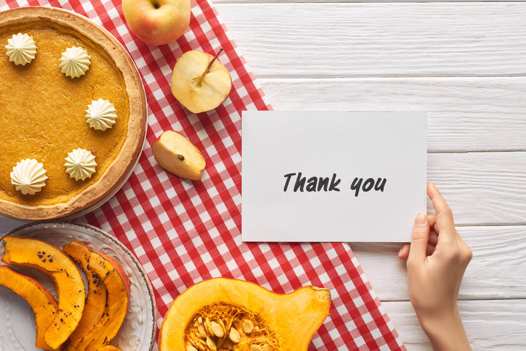 abgeschnittene Ansicht einer Frau mit Dankeskarte in der Nähe von Kürbiskuchen auf einem weißen Holztisch mit Äpfeln - Foto, Bild