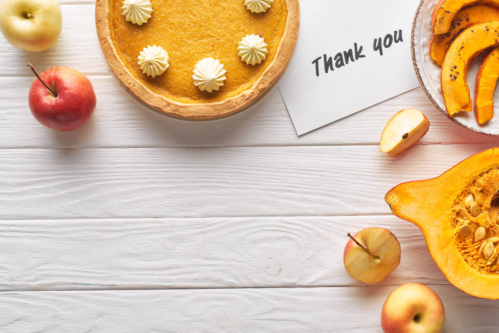 vista superior de delicioso pastel de calabaza con tarjeta de agradecimiento en la mesa blanca de madera con manzanas
 - Foto, Imagen